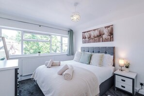 A bedroom with a bed, a bedside table, a lamp, a window, and a painting on the wall. - *NEW* 3BR Home | Driveway | Garden | Pool Table (West Midlands)