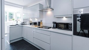 A modern kitchen with white cabinetry, a stainless steel range hood, a built-in microwave, and a window providing natural light. - *NEW* 3BR Home | Driveway | Garden | Pool Table (West Midlands)
