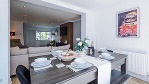 A dining area with a table set for four, a sofa, a television, and a framed picture on the wall. - *NEW* 3BR Home | Driveway | Garden | Pool Table (West Midlands)