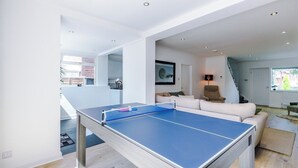 A modern living room with a ping pong table, a sofa, and a staircase leading to another level. - *NEW* 3BR Home | Driveway | Garden | Pool Table (West Midlands)