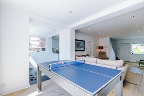 Ein modernes Wohnzimmer mit Tischtennisplatte, einer Couch und einer Treppe, die in eine weitere Ebene führt.