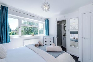 A bedroom with a bed, a dresser, a window with curtains, a door, and a wall-mounted light fixture. - *NEW* 3BR Home | Driveway | Garden | Pool Table (West Midlands)