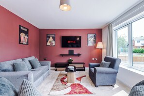 Ein modernes Wohnzimmer mit einem großen Fernseher, roten Wänden und Blick durch ein großes Fenster.