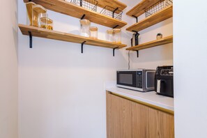 A kitchen with wooden shelves holding jars and a microwave on the counter. - NEW Relaxing 4BR House with Free WIFI & Parking (Bramhall)