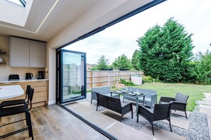 Una cocina moderna con comedor, una amplia puerta corrediza de vidrio que da a un jardín trasero con mobiliario exterior.