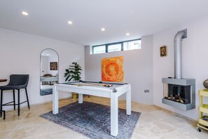 Ein modernes Wohnzimmer mit Billardtisch, Kamin und großem Fenster.