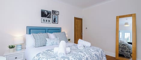 A bedroom with a bed, bedside tables, a mirror, and framed pictures on the wall.