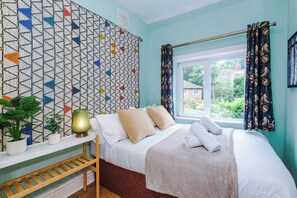 Ein Schlafzimmer mit Wandmuster, einem Fenster mit Vorhängen, einem Nachttisch mit Lampe und einem Bett mit Kissen und Decke.