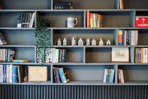 A bookshelf with various books, a framed picture, and a small plant. - *NEW* Funky 4BR Home | Sleeps 8 | Driveway | PS4 (Greater Manchester)