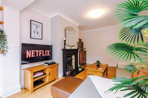 A living room with a flat-screen TV, wooden furniture, a fireplace, and a large plant. - *NEW* Funky 4BR Home | Sleeps 8 | Driveway | PS4 (Greater Manchester)