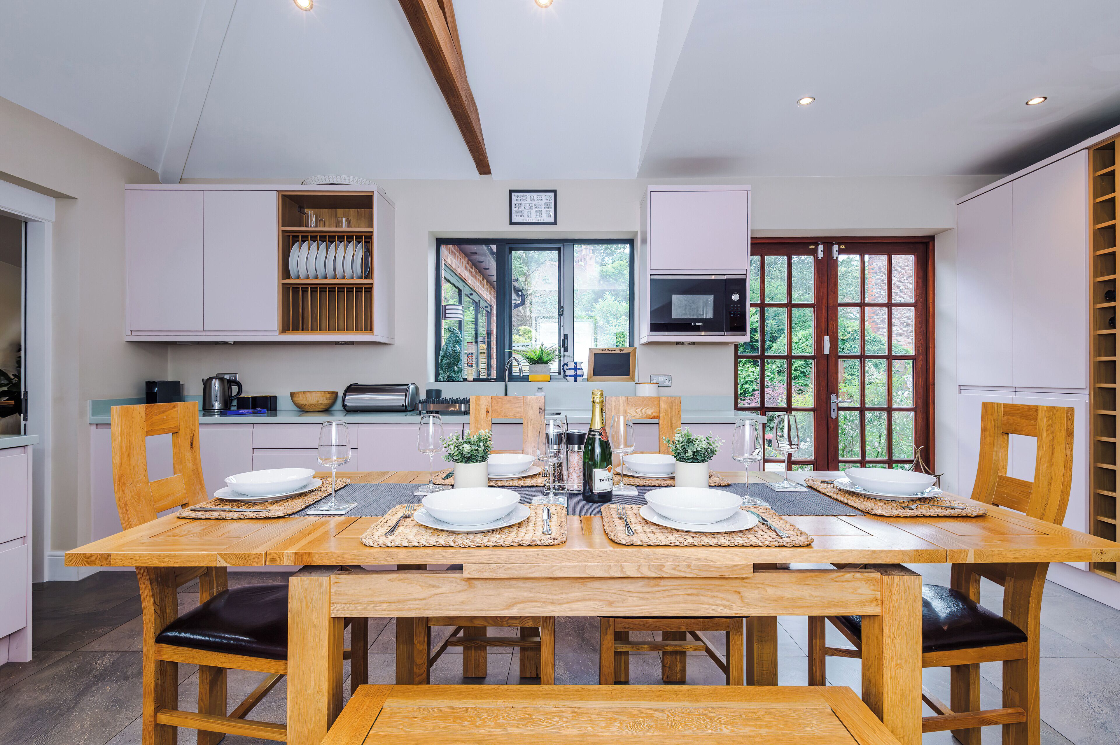 A modern kitchen with white cabinets, a Bosch microwave, and a dining area set with white plates and glasses.