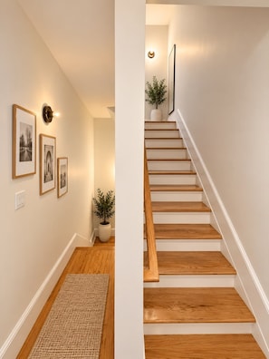 A staircase with wooden steps and white walls, a wall-mounted light fixture, and framed pictures on the wall. - Huge NYC Townhouse Near High Line & Meatpacking (New York)