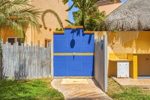 A gated entrance with a blue door, a wooden fence, and a thatched-roof structure. - Relaxing Family 2BR Condo / Walk to Beach & Pool (El Pescadero)