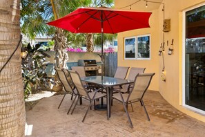 Eine Terrassenanlage im Freien mit Tisch, Stühlen, einem roten Sonnenschirm und einem Grill.