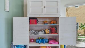 Ein weißes Schränkchen mit mehreren Regalböden, das verschiedene Gegenstände wie Taschen, einen Ball und gefaltete Kleidung beherbergt.