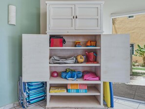 Ein weißes Schränkchen mit mehreren Regalböden, das verschiedene Gegenstände wie Taschen, einen Ball und gefaltete Kleidung beherbergt.