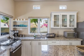 A kitchen with a granite countertop, stainless steel appliances, white cabinetry, and a window with a view of pink flowers. - Relaxing Family 2BR Condo / Walk to Beach & Pool (El Pescadero)