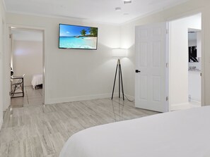 A bedroom with a bed, a desk, a chair, a floor lamp, and a TV on the wall. - Centric Vacation Home with Tiny House near Beaches (Tampa)