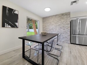 A modern kitchen with a marble floor, a stainless steel refrigerator, and a dining table with clear chairs. - Centric Vacation Home with Tiny House near Beaches (Tampa)