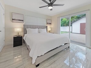 A modern bedroom with a large bed, two bedside tables with lamps, a ceiling fan, and a sliding glass door leading to an outdoor area. - Centric Vacation Home with Tiny House near Beaches (Tampa)