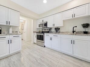 A modern kitchen with white cabinets, a microwave, an oven, and a sink. - Centric Vacation Home with Tiny House near Beaches (Tampa)