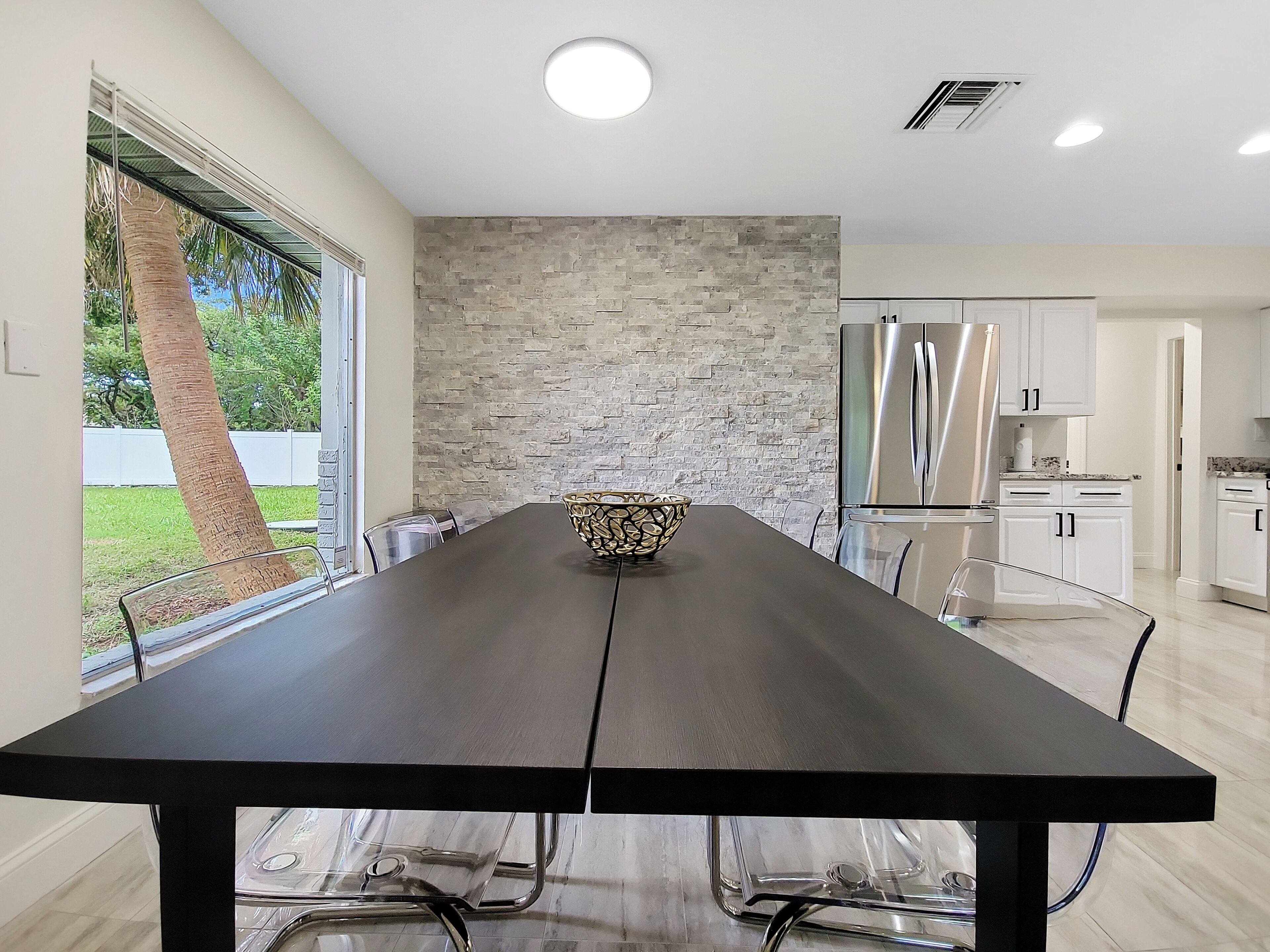 A modern kitchen with a stone backsplash, stainless steel appliances, and a dining area with a long table and chairs.