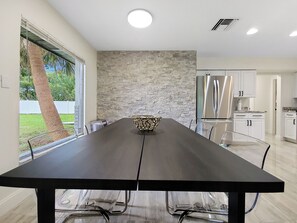 A modern kitchen with a stone backsplash, stainless steel appliances, and a dining area with a long table and chairs. - Centric Vacation Home with Tiny House near Beaches (Tampa)