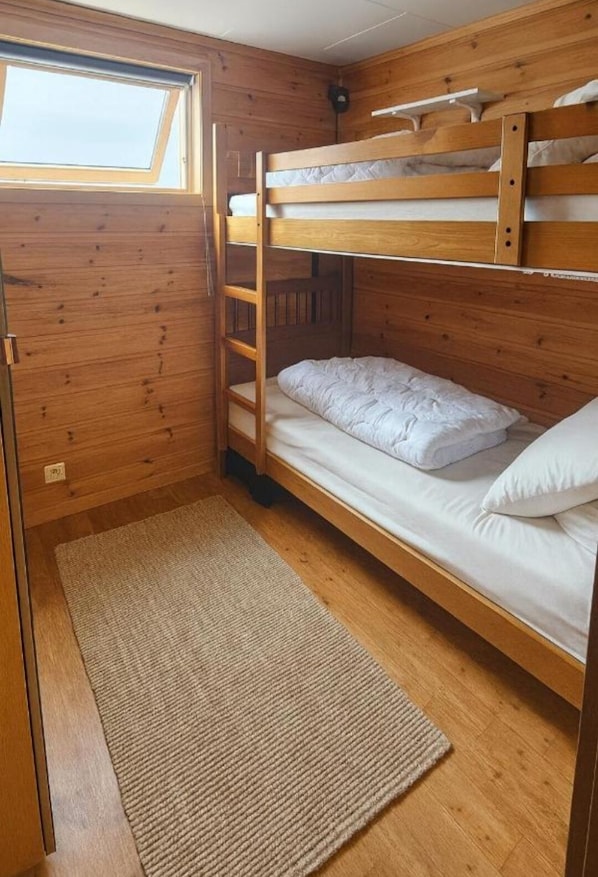 A bunk bed room with a skylight, wooden walls, and a rug.