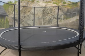 A trampoline with a safety net, set against a rocky landscape backdrop.
