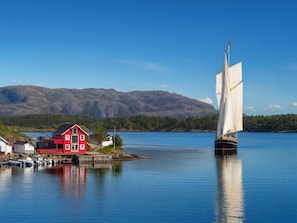 A calm lake with a sailboat, a red house, and mountains in the background.