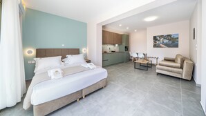 Habitació d'hotel moderna amb un llit, un sofà, una taula petita i una zona de cuina al fons.