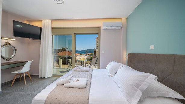 Una habitació d'hotel amb llit, televisió, escriptori, cadira i un balcó amb taula i cadires.