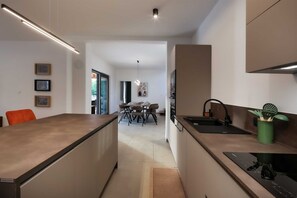 Eine moderne Küche mit einer Kochinsel, einem Essbereich mit Tisch und Stühlen sowie Blick in den angrenzenden Wohnraum.