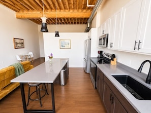 A modern kitchen with a central island, stainless steel appliances, and a wooden ceiling.