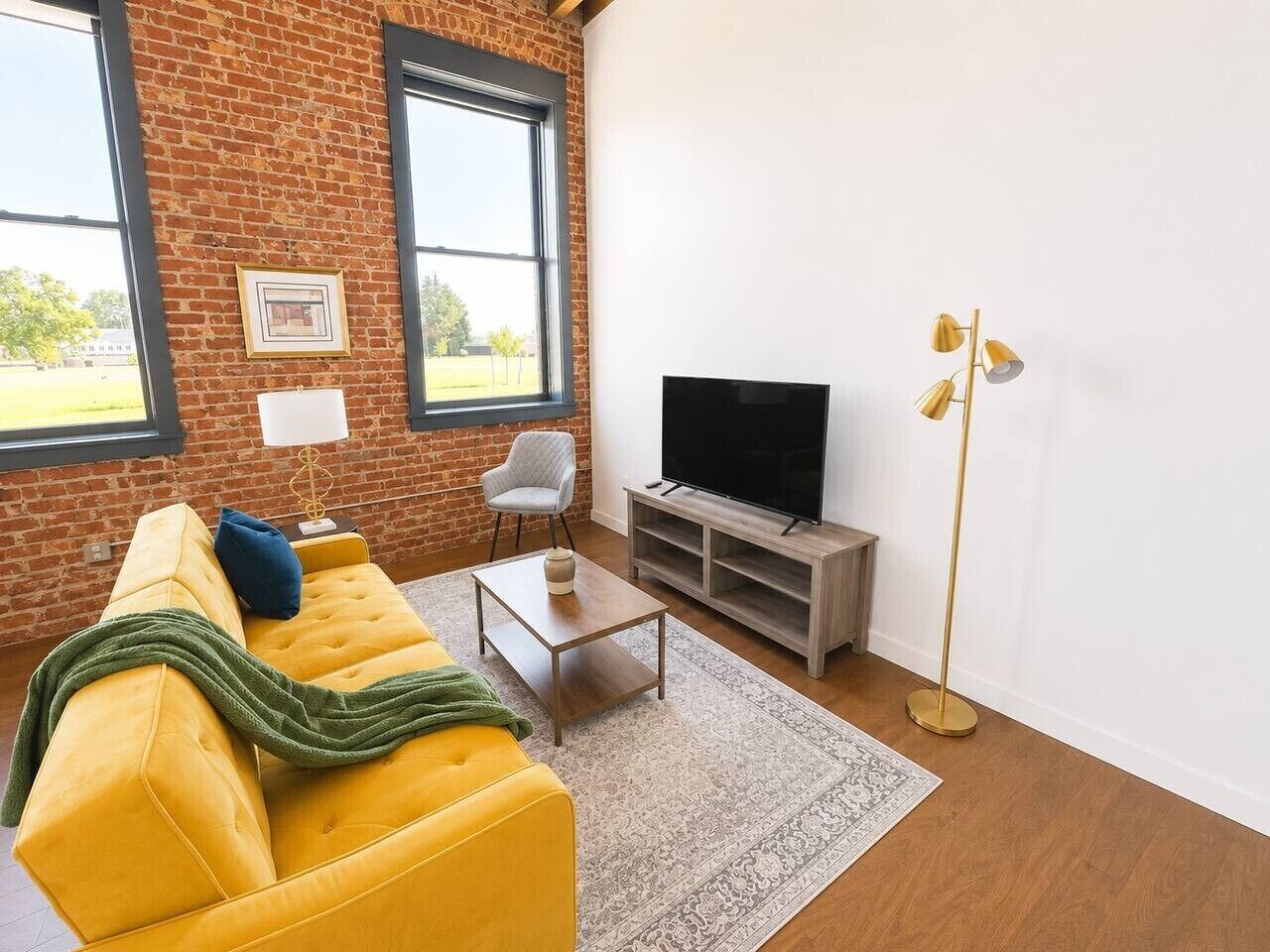 A living room with a yellow sofa, a television, a floor lamp, and a brick wall.
