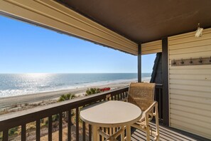 Een balkon met uitzicht op het strand, een tafel, stoelen en een kapstok.