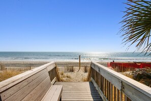 Ein Holzsteg führt zu einem Strand mit freiem Blick auf das Meer.