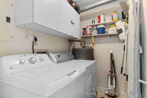 A laundry area with a front-loading washer and dryer, a water heater, and a shelf with cleaning supplies. - Sun-kissed Dunes: 2-bedroom condo Oceanfront; pool sleeps 6 (Myrtle Beach)