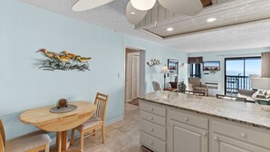 A kitchen with a wooden table and chairs, a ceiling fan, and a view of the ocean. - Sun-kissed Dunes: 2-bedroom condo Oceanfront; pool sleeps 6 (Myrtle Beach)