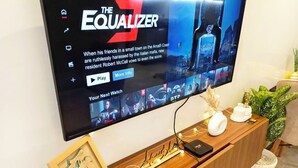 Una TV a schermo piatto montata su un mobiletto in legno, con una cornice e oggetti decorativi.