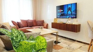 Un soggiorno con divano, tavolino e televisore a parete che mostra un programma.