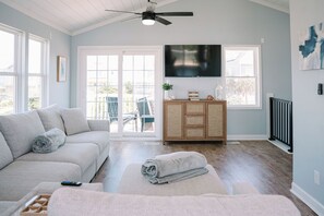 Ein Wohnzimmer mit einer Couch, einem Fernseher, einem Deckenventilator und Blick durch eine Glastür.