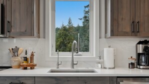 A modern kitchen with wooden cabinets, a stainless steel dishwasher, and a window with a view of trees.