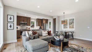 A modern living space with a grey sectional sofa, a round coffee table, and a dining area with a black chair and table.