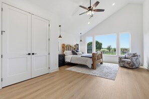A bedroom with a bed, a chair, a ceiling fan, and large windows. - 3-bedroom+office luxury home on the edge of GlenRose, TX. Private. Pickleball. (Rainbow)