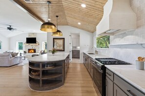 A modern kitchen with a central island, wooden ceiling, and a stone fireplace. - 3-bedroom+office luxury home on the edge of GlenRose, TX. Private. Pickleball. (Rainbow)
