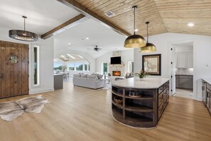 Uma sala de estar ampla com uma ilha grande, piso de madeira e teto alto com vigas aparentes.