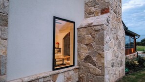 A stone exterior wall with a window revealing an interior room with a fireplace and a sofa. - 3-bedroom+office luxury home on the edge of GlenRose, TX. Private. Pickleball. (Rainbow)