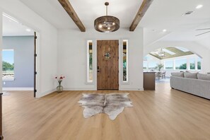 A spacious living area with a wooden floor, a large grey sofa, a wooden door with a glass panel, and a hanging light fixture. - 3-bedroom+office luxury home on the edge of GlenRose, TX. Private. Pickleball. (Rainbow)