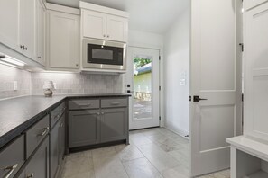 A kitchen with white cabinets, a microwave, and a tiled backsplash. - 3-bedroom+office luxury home on the edge of GlenRose, TX. Private. Pickleball. (Rainbow)